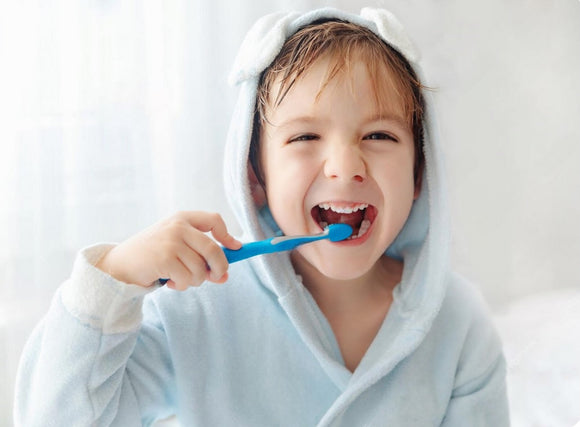 Child brushing teeth with blue toothbrush, smiling in cozy bathrobe, promoting healthy dental hygiene.