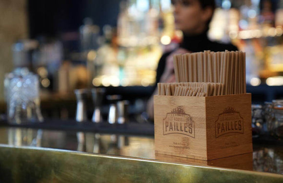 Eco-friendly sugarcane straws displayed in a wooden holder at a bar, highlighting sustainable beverage options.