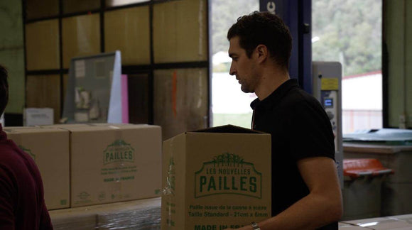 Opérateur manipulant un carton de pailles en bagasse dans un site de production.