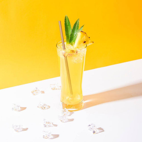 Cocktail rafraîchissant avec paille en bagasse, garni d'ananas et de menthe, sur fond jaune vif.